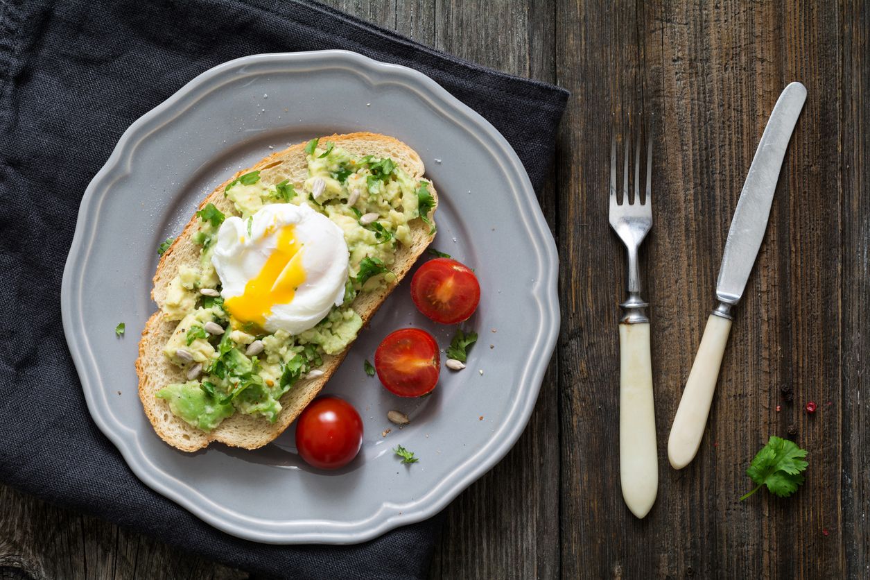 Toast de blé entier avec guacamole, œuf poché et tomates cerises.